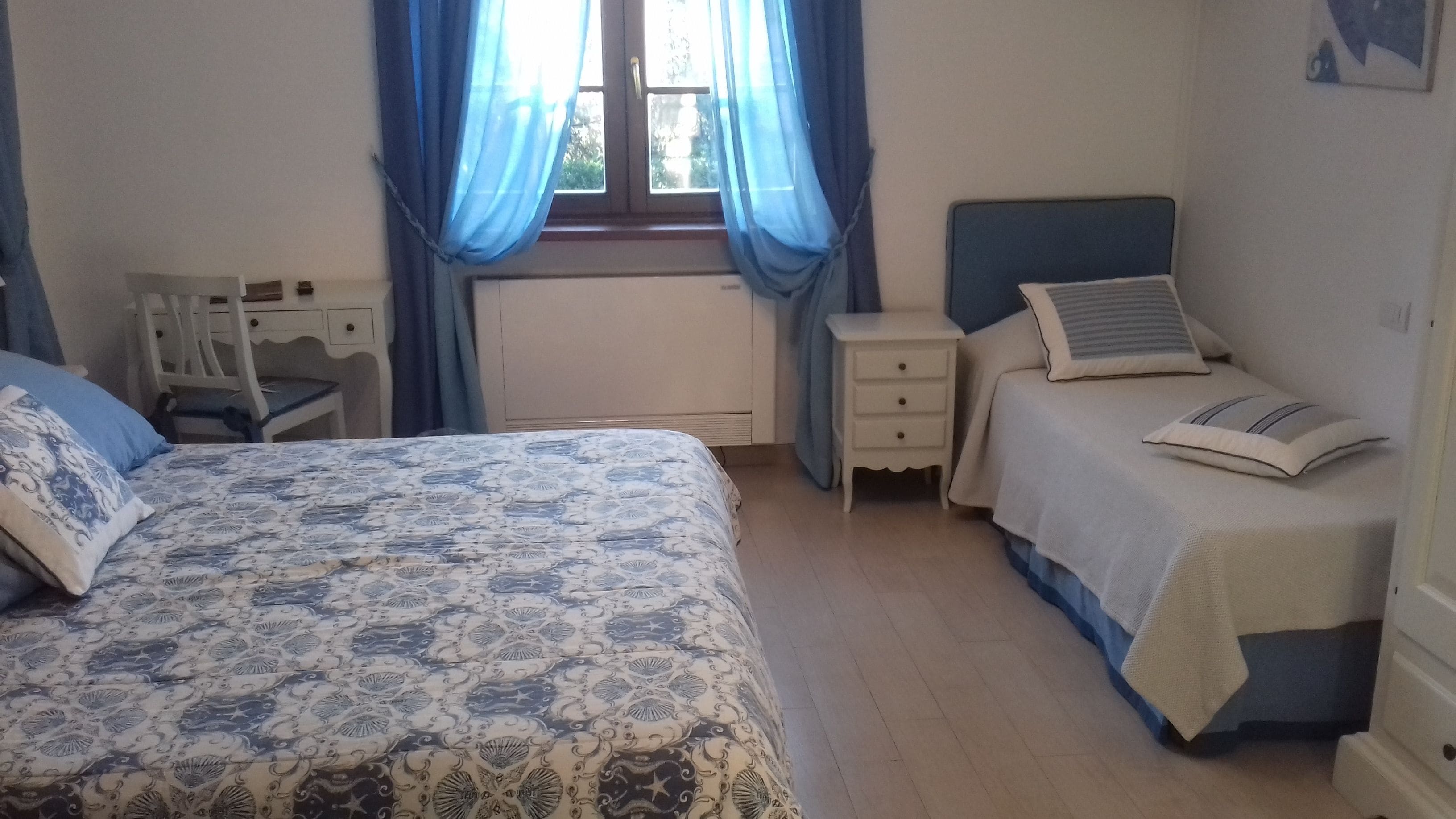 Een slaapkamer met een groot bed, een kleiner bed, een bureau en een stoel.