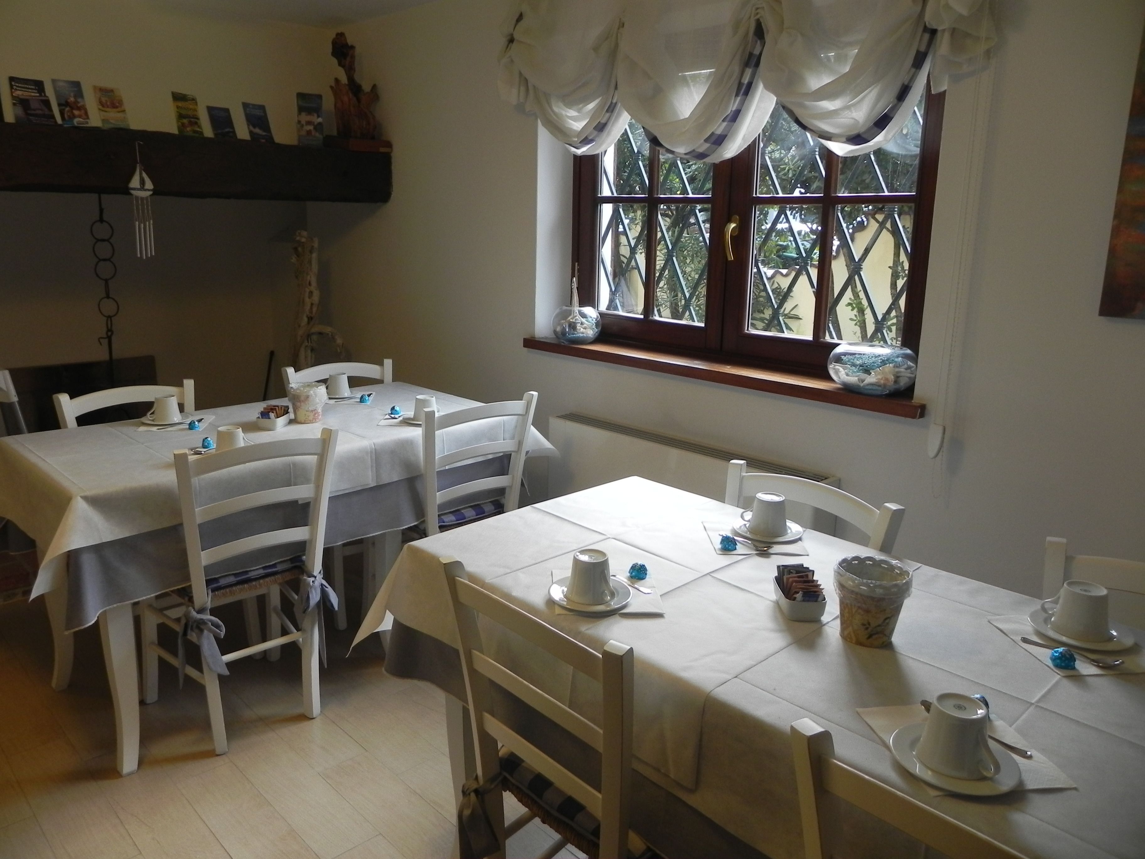 A dining area with two tables set for a meal, white chairs, and a window with curtains.