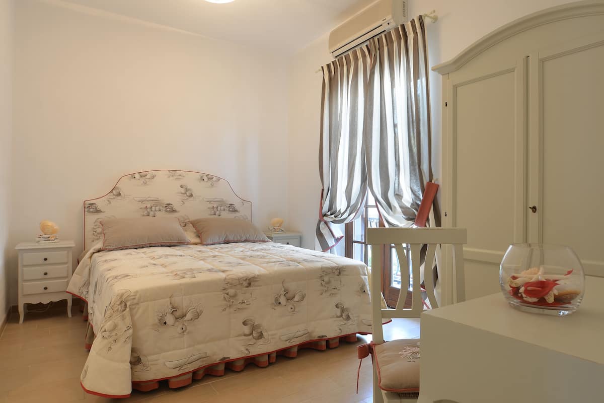 A bedroom with a bed, a bedside table, a chair, and a glass fishbowl on a dresser.