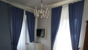 A bedroom with a bed, a nightstand, a lamp, a dresser, a television, and curtains. - Residenza D'Epoca Villa Agnolaccio (Pistoia)