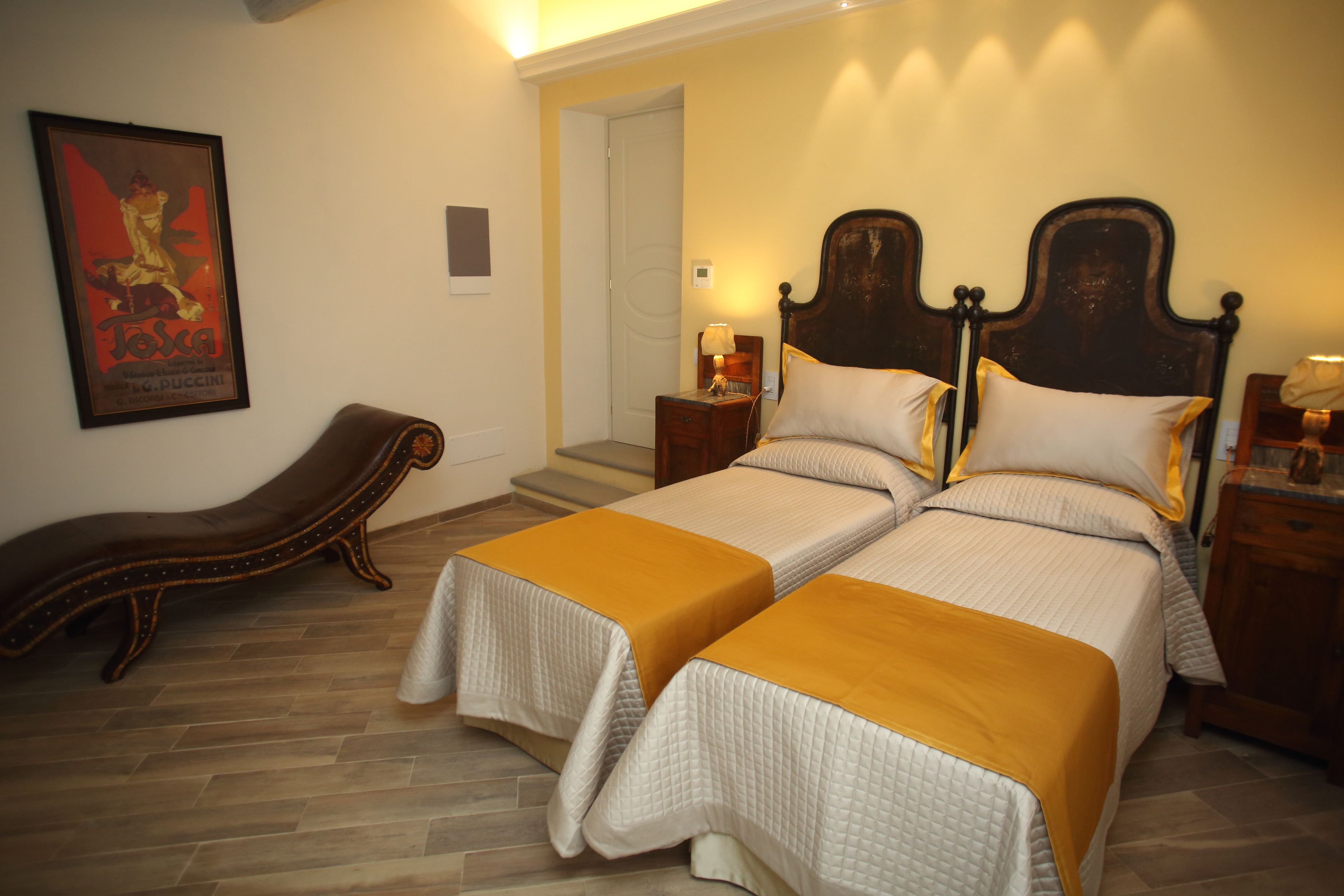 Habitación de hotel con dos camas, un banco de madera, un cartel en la pared y una puerta que da a otra habitación.