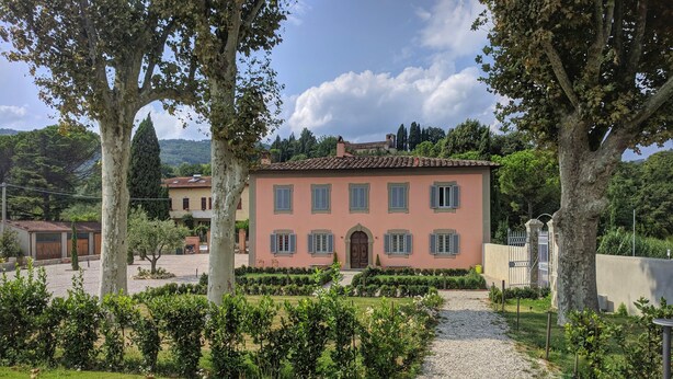 A pink villa with a gravel path leading to the entrance, surrounded by well-maintained hedges and trees. - Residenza D'Epoca Villa Agnolaccio (Pistoia)