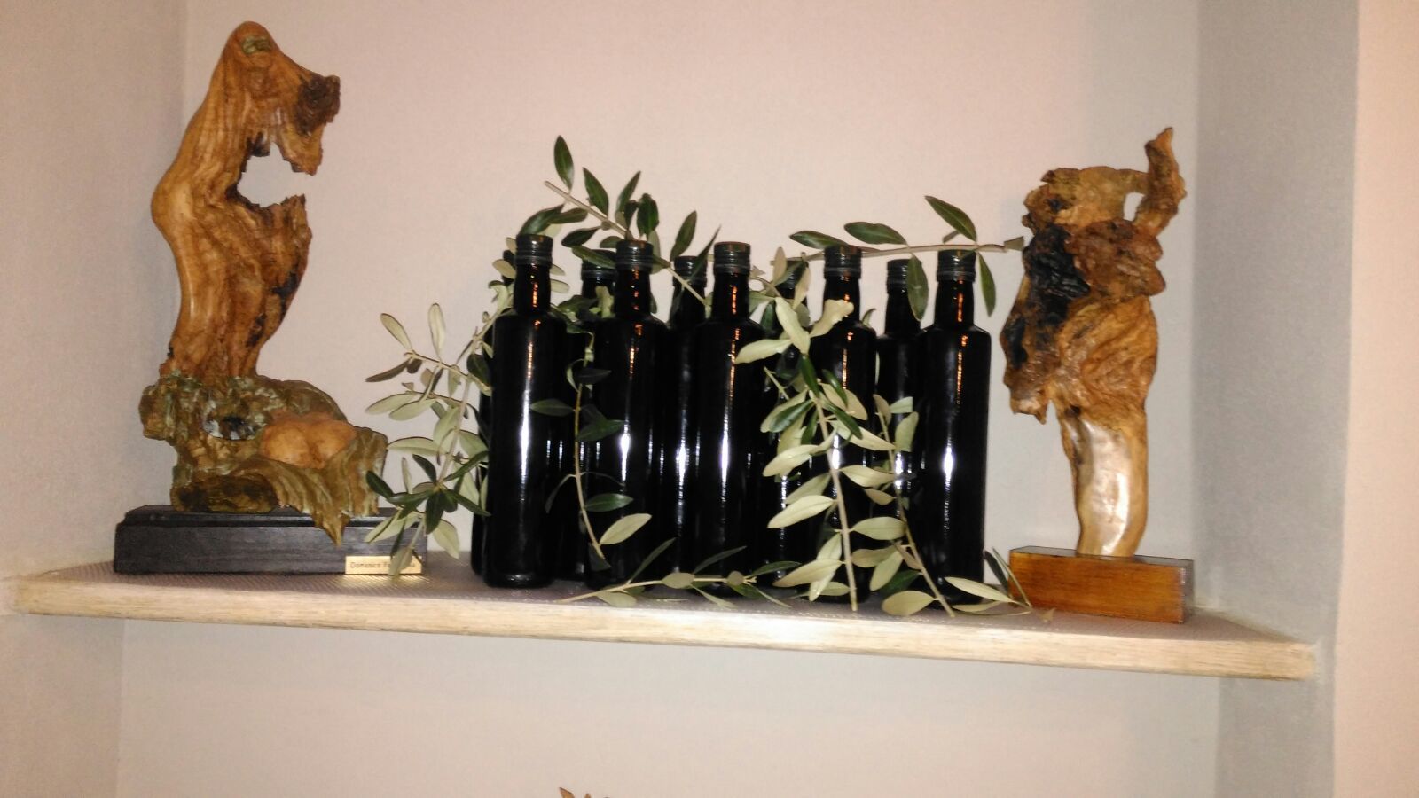 Uma prateleira com garrafas de vinho e duas esculturas de madeira.