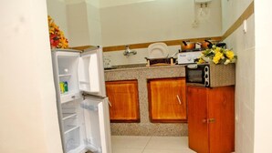 A compact kitchen with a refrigerator, wooden cabinets, a microwave, and a stove. - Residence Rom 4 Treicheville (Abidjan)