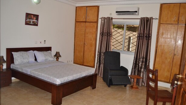 A bedroom with a bed, a chair, a wardrobe, and an air conditioning unit. - Residence Rom 4 Treicheville (Abidjan)