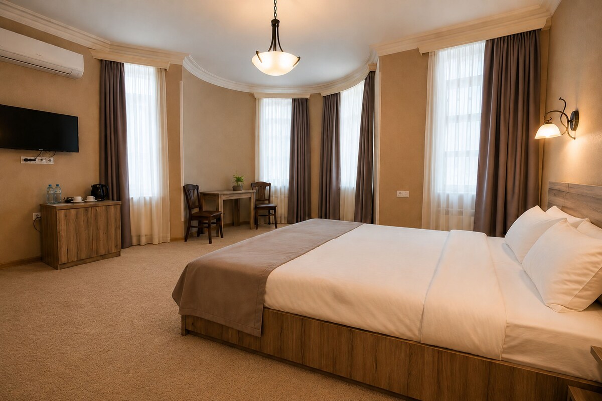 A hotel room with a large bed, a desk, a chair, a television, and a wall-mounted light fixture.