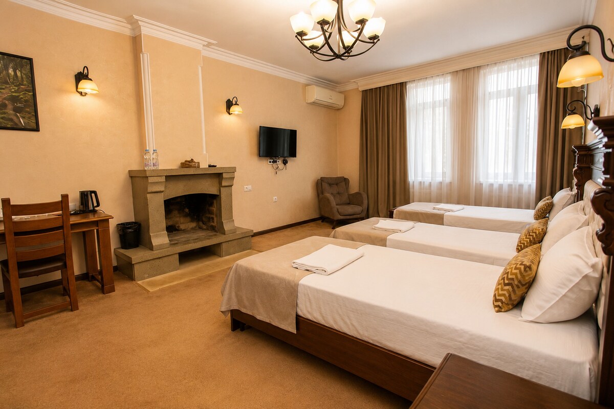 A hotel room with two beds, a fireplace, a television, and a desk with a chair.