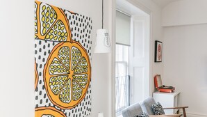 A modern living room with a large fruit-themed artwork, a white vase, and a seating area with patterned cushions. - Urban Quarters Serviced Apartments (Dundee)