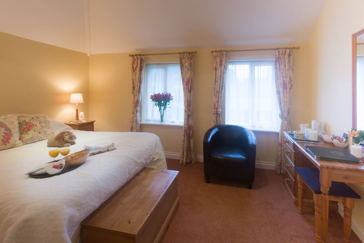A hotel room with a bed, a desk, a chair, a nightstand, and a window with curtains.