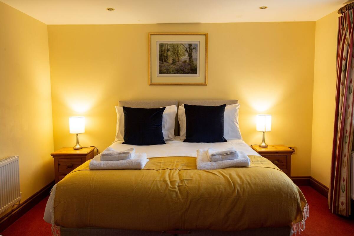 A hotel room with a large bed, two bedside lamps, a framed picture on the wall, and a window with curtains.