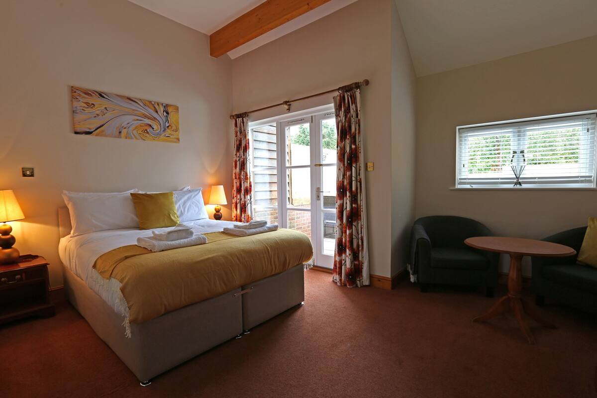 A bedroom with a bed, two bedside lamps, a window with blinds, a chair, and a table.