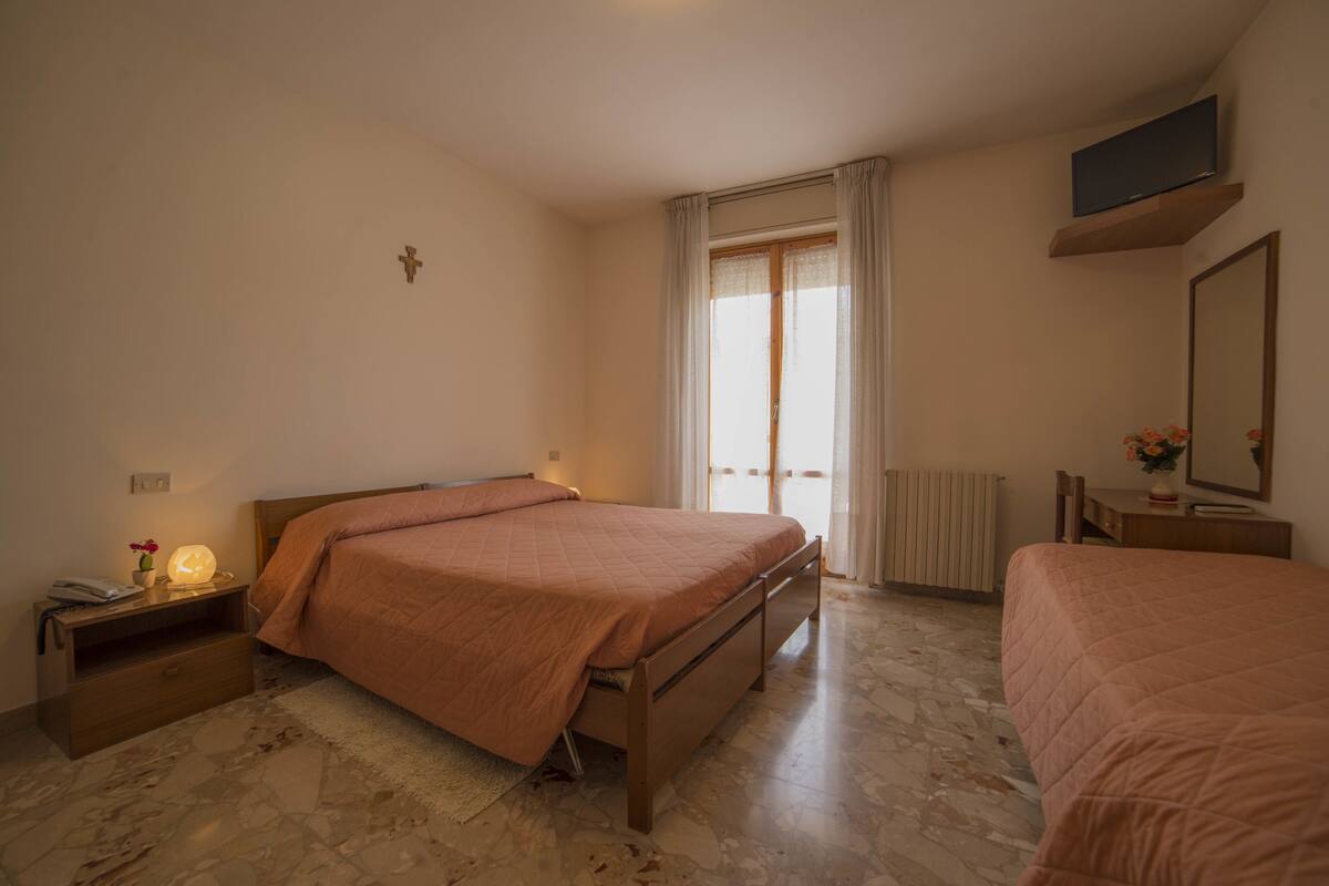 Een slaapkamer met een bed, nachtkastje, lamp en een televisie op een plank.