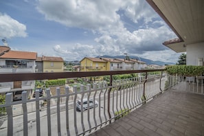 A balcony with a view of a street, buildings, and mountains in the distance. - Hotel Santa Maria (Assisi)