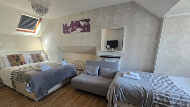A bedroom with two beds, a sofa, a ceiling light, a window, and a TV. - Adams Guest House (Oxford)