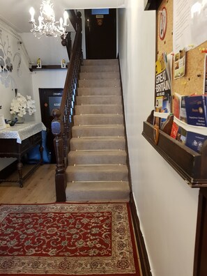 Stairs lead to an area, flanked by a chandelier and a corkboard with pinned items.