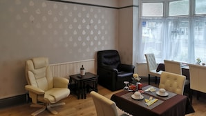 A dining area with a table set for two, a black leather chair, a cream leather chair, and a chandelier. - Adams Guest House (Oxford)