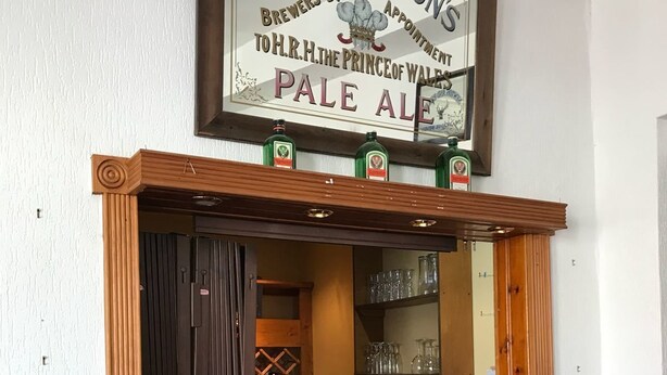 Una zona de bar con un cartel que dice "Worthington's Pale Ale" y una barra de madera con taburetes.
