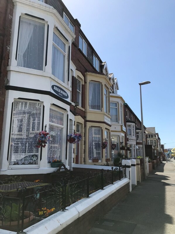 A row of traditional terraced houses with bay windows, one of which has a sign for 'Beckwood Hotel'.