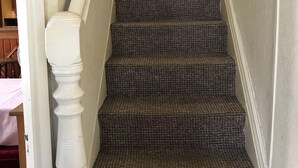 Una escalera con alfombra texturizada y balaustres blancos.
