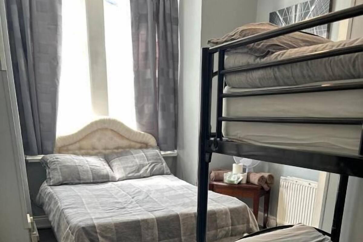 A bedroom with two beds, one with a headboard and one with a bunk. There is a small table with a bottle and a tissue box.