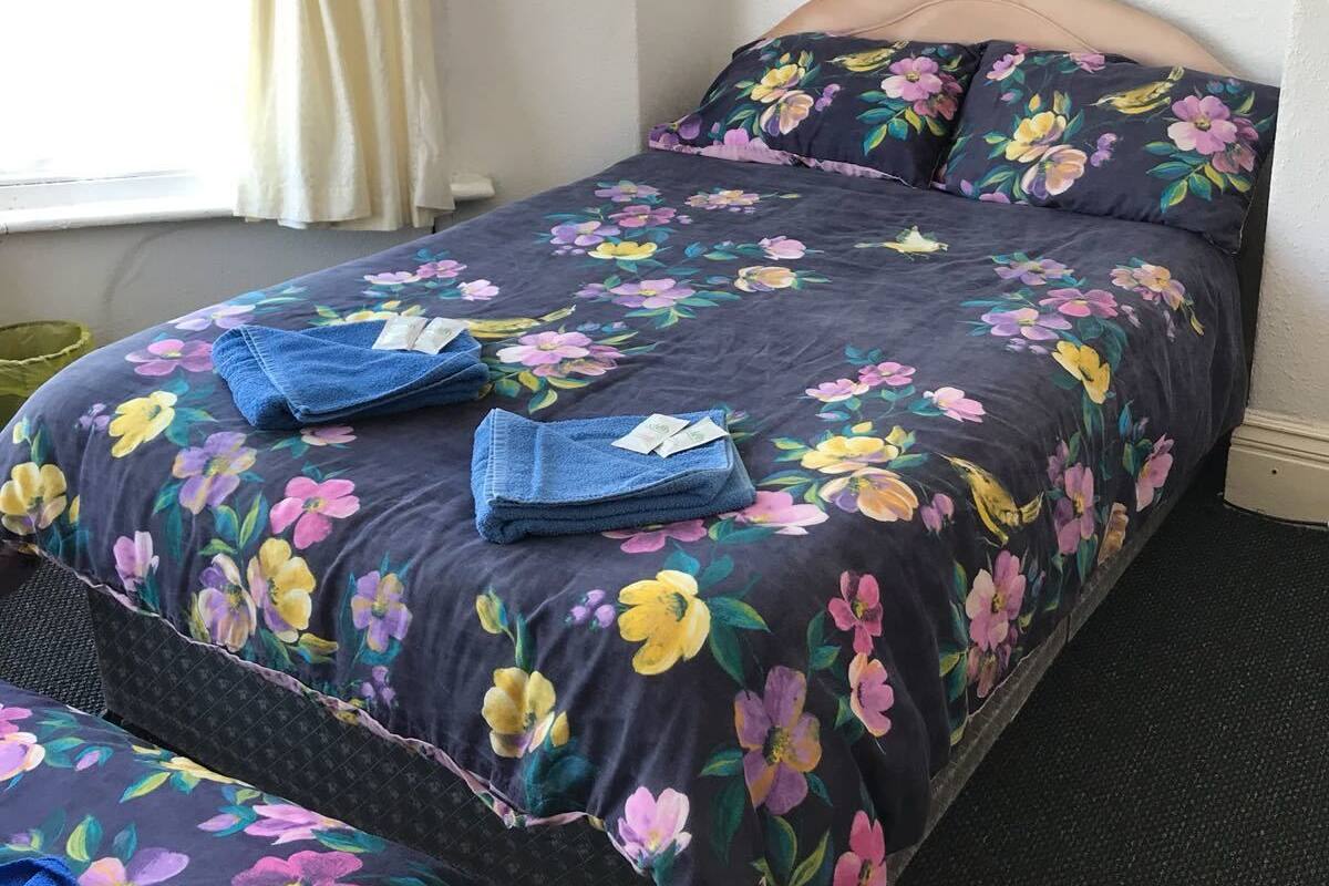A neatly made bed with floral bedding, a headboard, and a window with curtains.