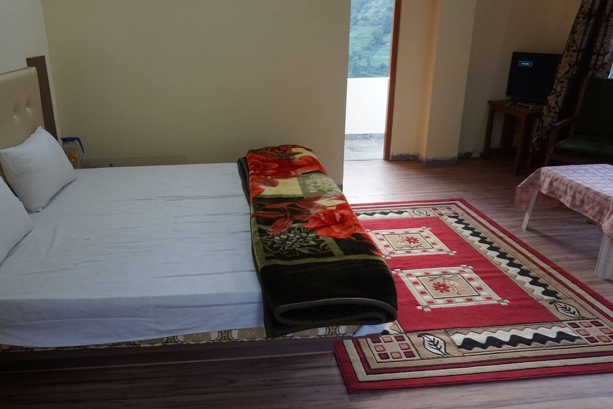 A neatly made bed with white linens, a floral blanket, and a red and beige patterned rug.