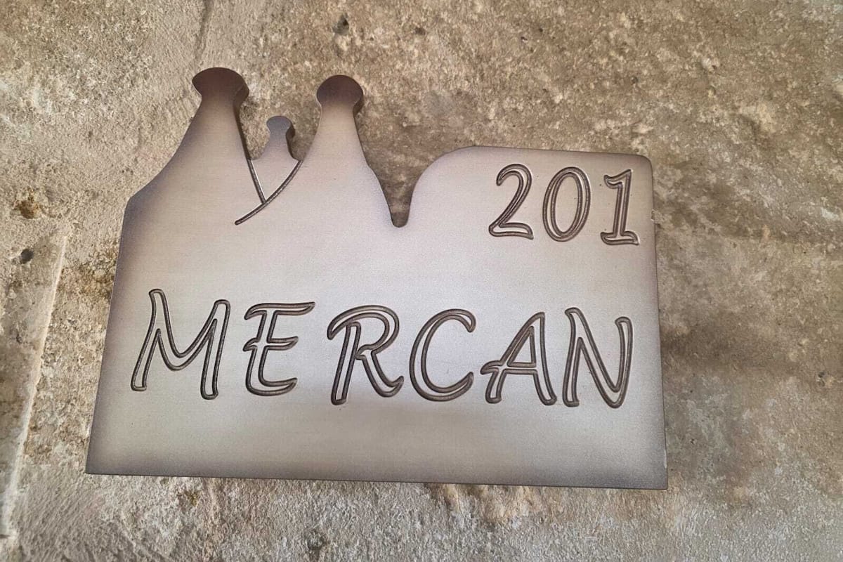 Una placa de metall amb la inscripció "201 MERCAN" sobre una paret de pedra amb relleu.
