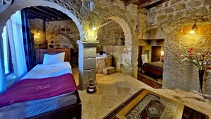 A stone-walled room with a bed, a small table, and a bench. - Cappadocia Antique House (Ürgüp)