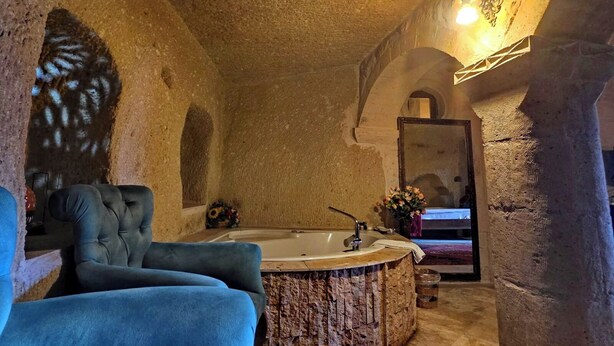 A stone-walled bathroom with a large bathtub, a blue chair, and a flower arrangement. - Cappadocia Antique House (Ürgüp)
