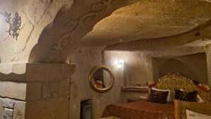A room with a stone ceiling and walls, a bed with a headboard, a mirror, and a small table. - Cappadocia Antique House (Ürgüp)