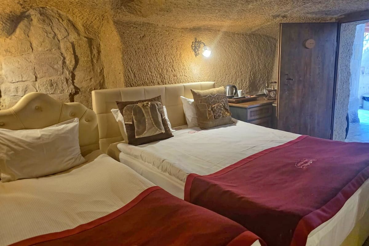 Habitació amb dos llits, una paret de pedra, una porta de fusta i una cambrera amb una làmpada.