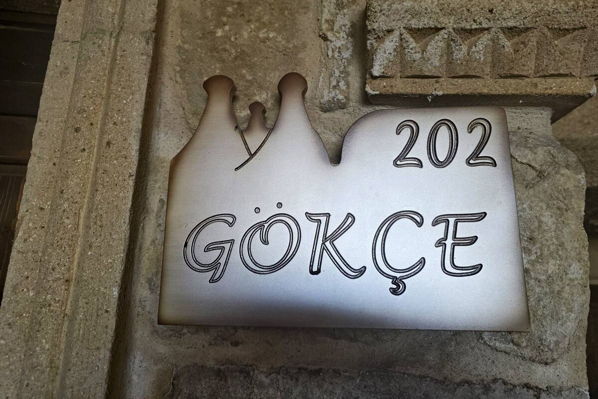 Una placa de metall amb el número 202 i el nom 'GÖKÇE' gravat, subjecta a una paret de pedra.