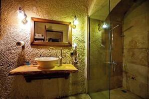 A bathroom with a stone wall, a wooden vanity with a large sink, a mirror, and a glass-enclosed shower.