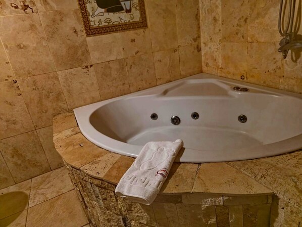 A bathroom with a freestanding bathtub, a towel, and a tiled wall with a decorative border. - Cappadocia Antique House (Ürgüp)