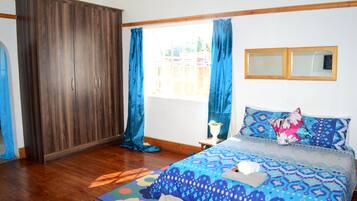 Un dormitorio con cama, armario, ventana con cortinas y una mesita con una planta.