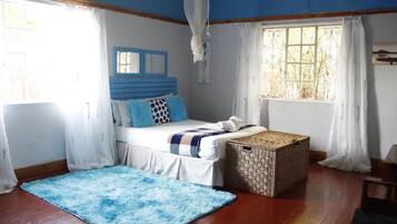 Ein Schlafzimmer mit einem Bett, einem blauen Kopfteil, einem Fenster mit weißen Vorhängen, einem Holzboden und einem blauen Teppich.