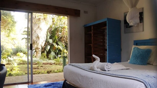A bedroom with a bed, a blue wardrobe, and a view of a garden through a sliding door. - Breeze Guest House (Bulawayo)