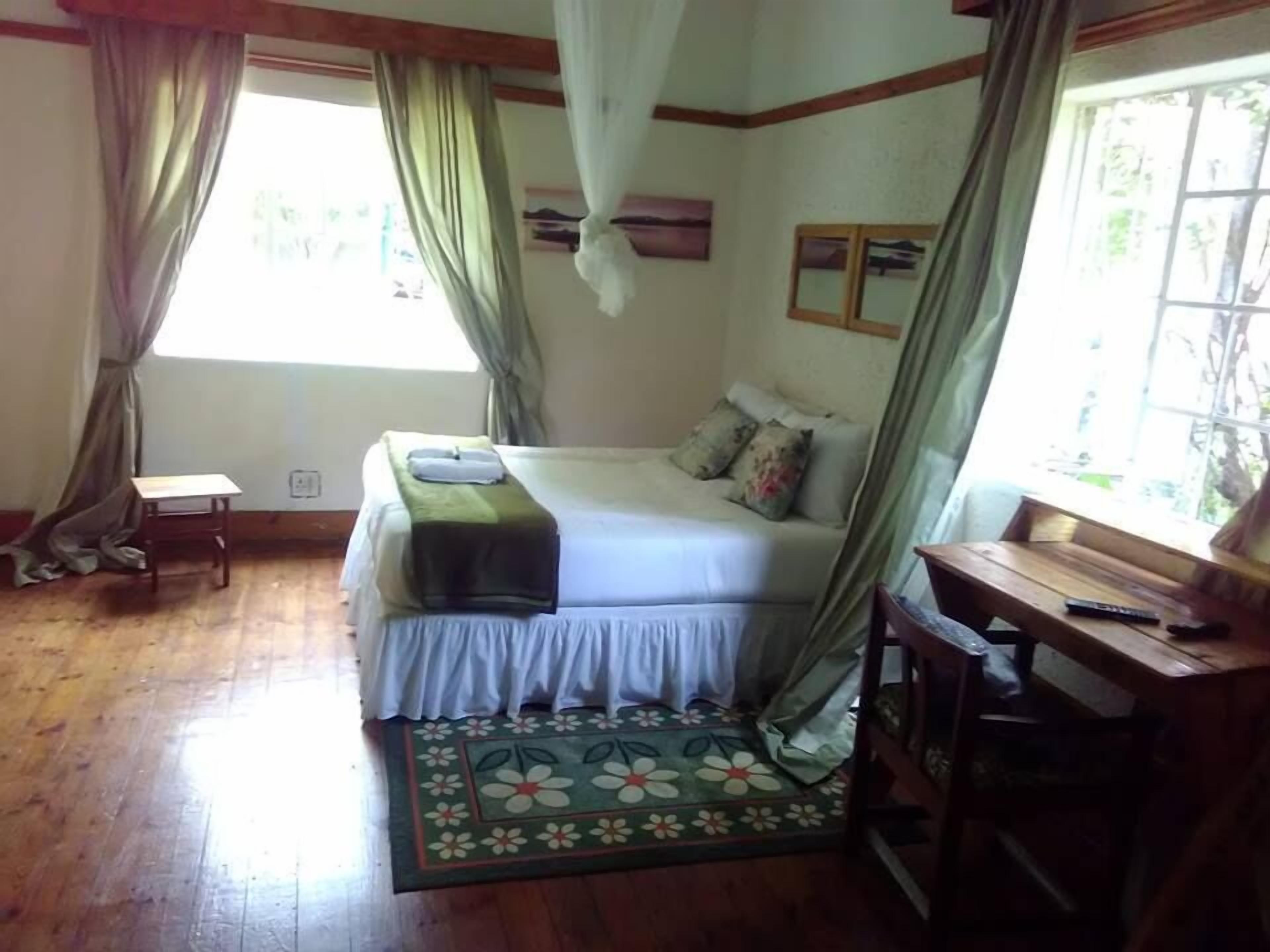 A bedroom with a bed, a small table, a desk, and a window with curtains.