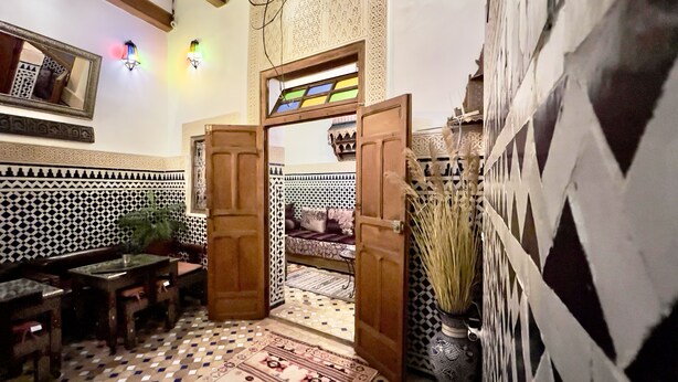 Un interior marroquí tradicional con una puerta de madera, azulejos estampados, un sofá y una zona de comedor.