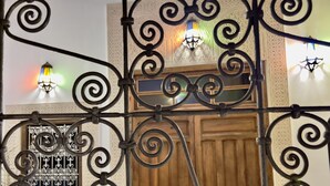 Una reja de hierro forjado con diseños intrincados, una puerta de madera y un muro con un panel decorativo y un accesorio de iluminación.