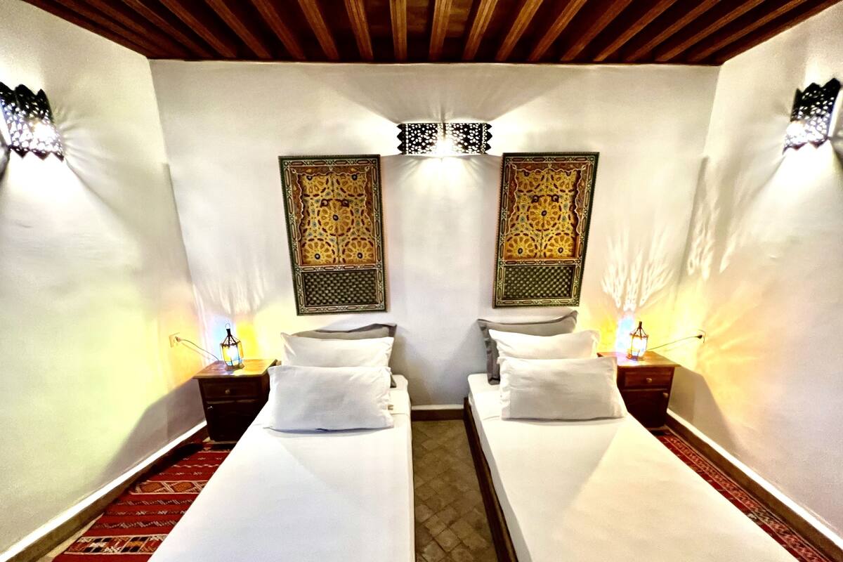 A room with two beds, a patterned wall hanging, and a red patterned carpet.