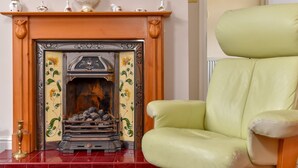 A room with a fireplace, a green armchair, and a patterned rug. - The Warren Guest House (Carlisle)