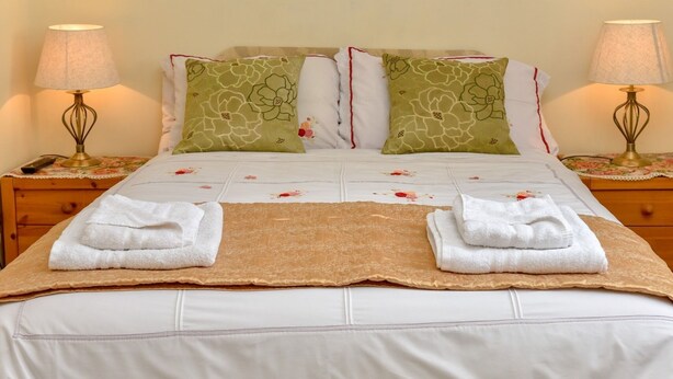 A neatly made bed with white linens, two green floral pillows, and two folded white towels. - The Warren Guest House (Carlisle)