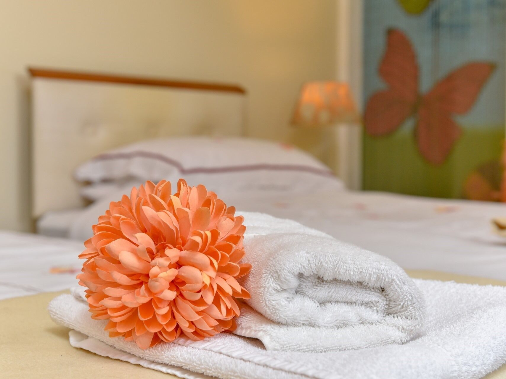 A neatly made bed with a folded white towel and a large orange flower.