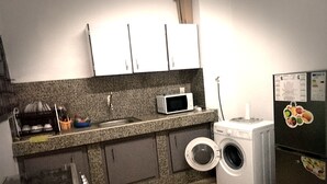 A compact kitchen with a microwave, washing machine, and a refrigerator with magnets. - Residence M&N Bounoumin (Abidjan)