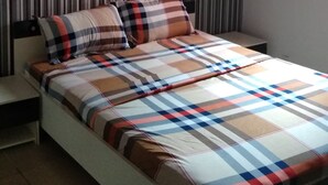 A bed with a plaid bedspread, a bedside table, and a wall with vertical stripes. - Residence M&N Bounoumin (Abidjan)