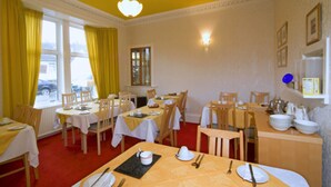 A dining area with multiple tables and chairs, yellow curtains, and a window with a view of the outside. - St. Annes Guest House (Oban)