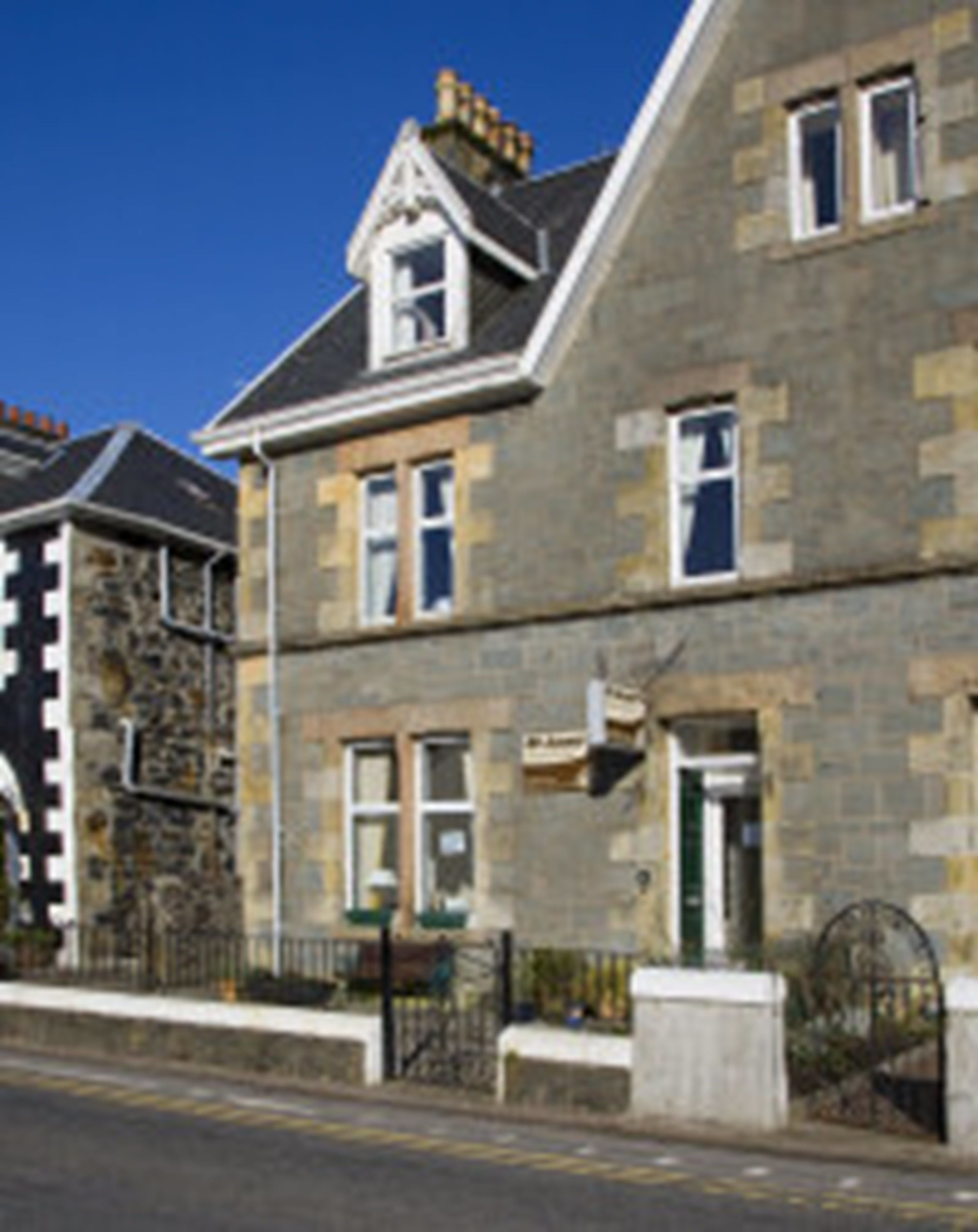 A two-story stone building with a traditional design, featuring a prominent chimney, multiple windows, and a gated entrance.