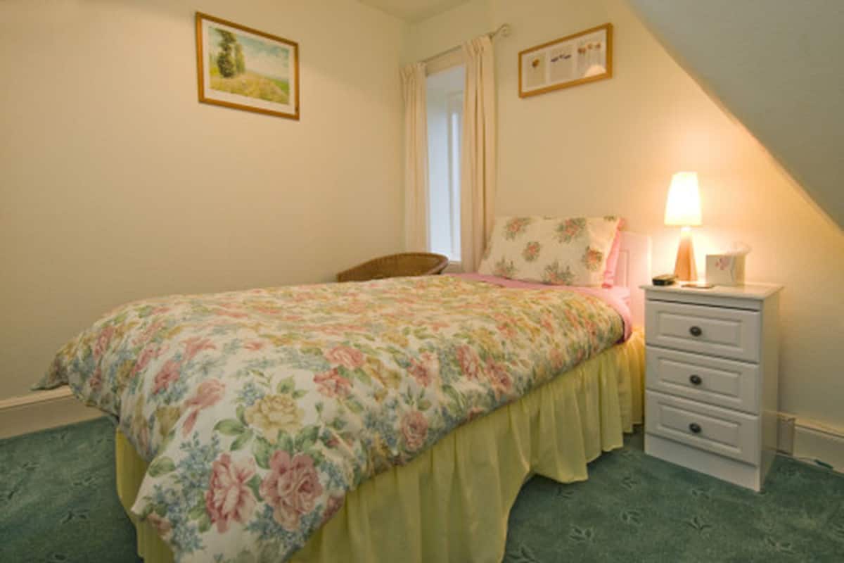A bedroom with a floral bedspread, a bedside lamp, and a white dresser.