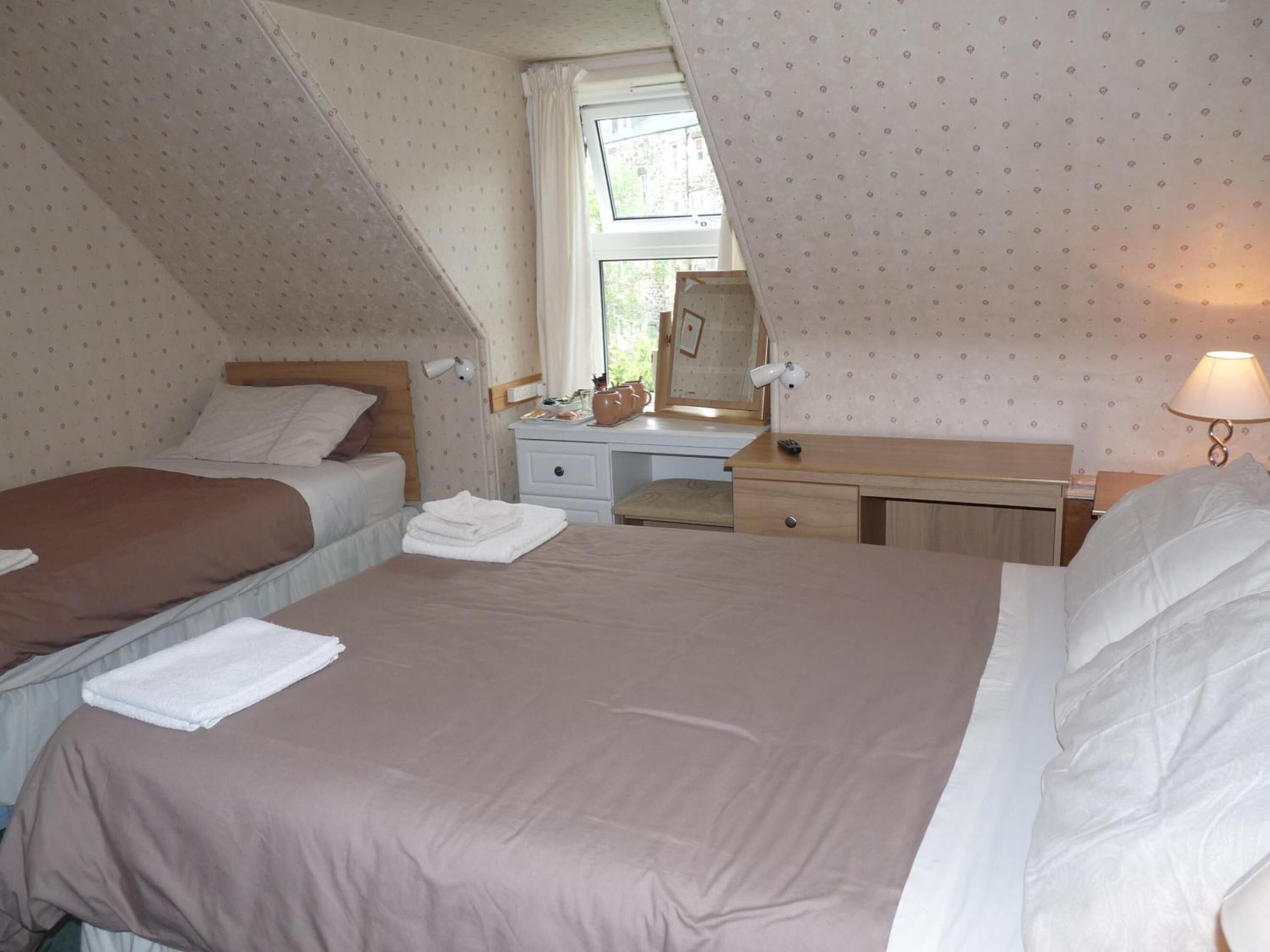 A bedroom with two beds, a desk, and a window.